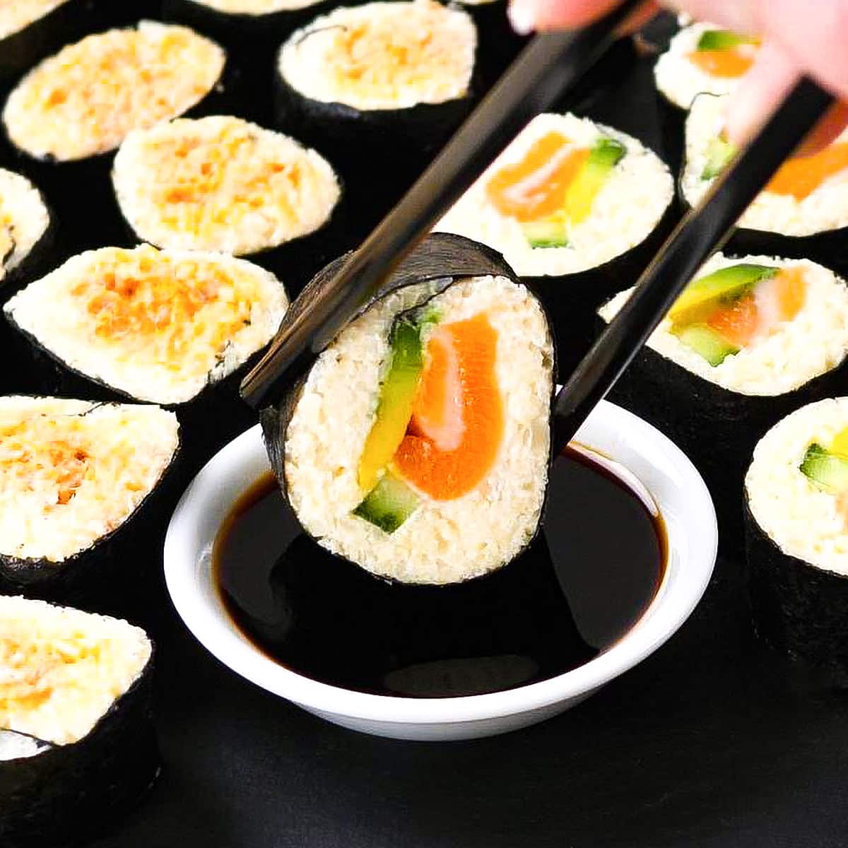 Keto sushi roll in chopsticks being dipped in tamari sauce.