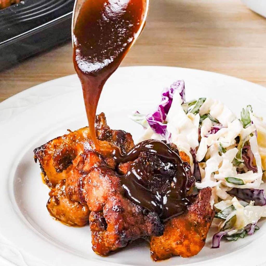 Keto BBQ sauce over chicken on a white plate with coleslaw.