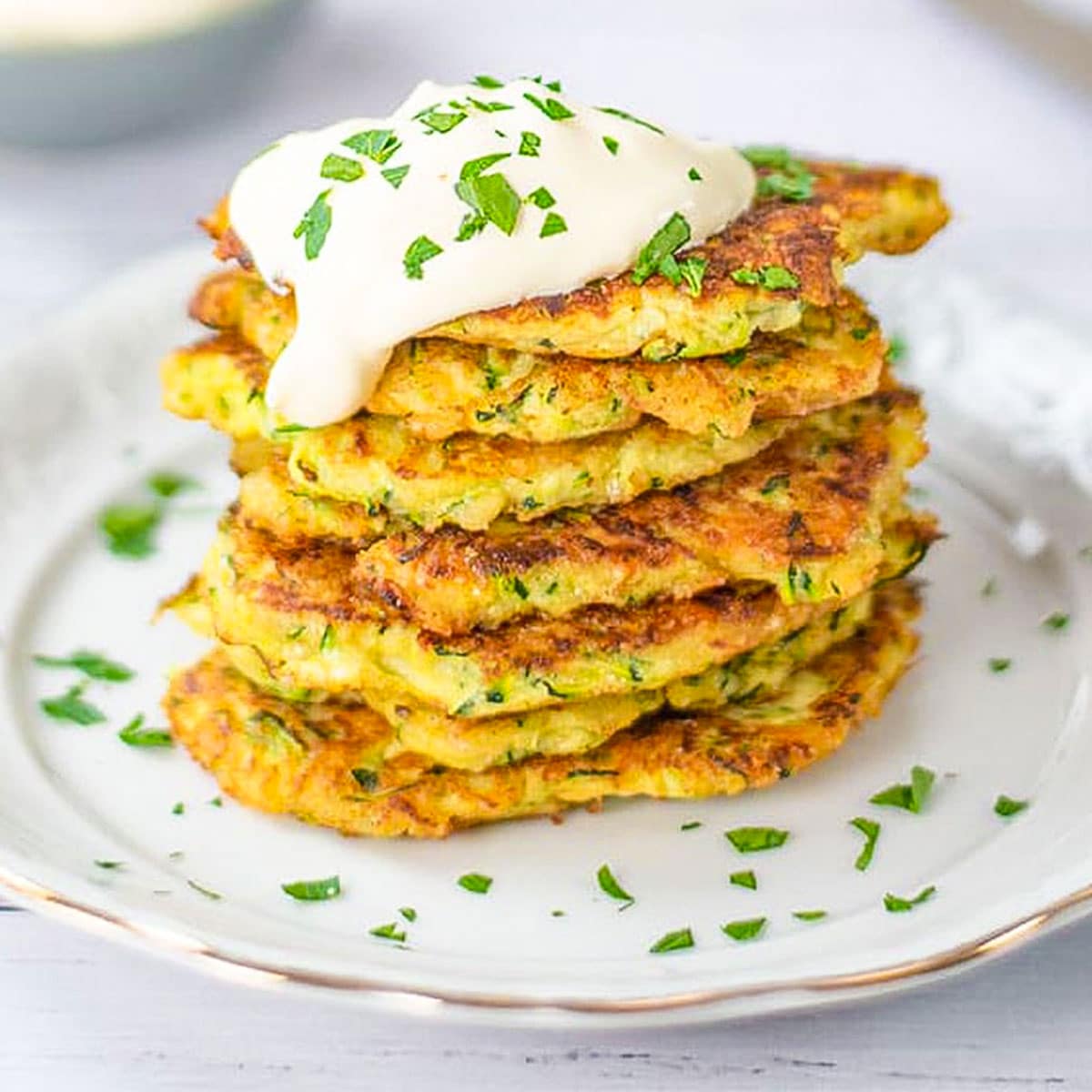 Keto zucchini fritters on a plate with sour cream.