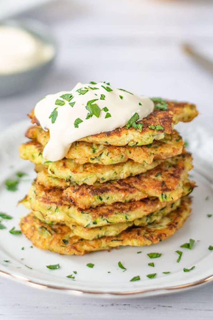 Six keto zucchini fritters stacked on a white plate.