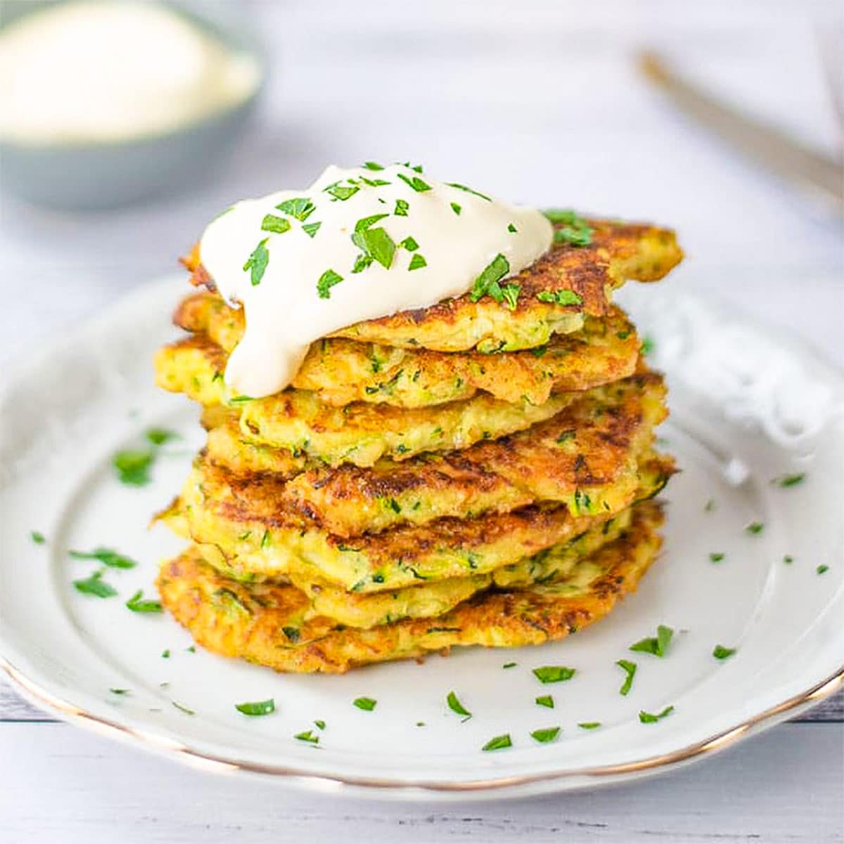 Keto zucchini fritters on a white plate topped with cream.
