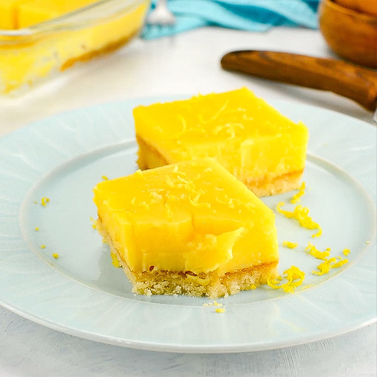 Two keto lemon bars on a plate one with a bite out of it.