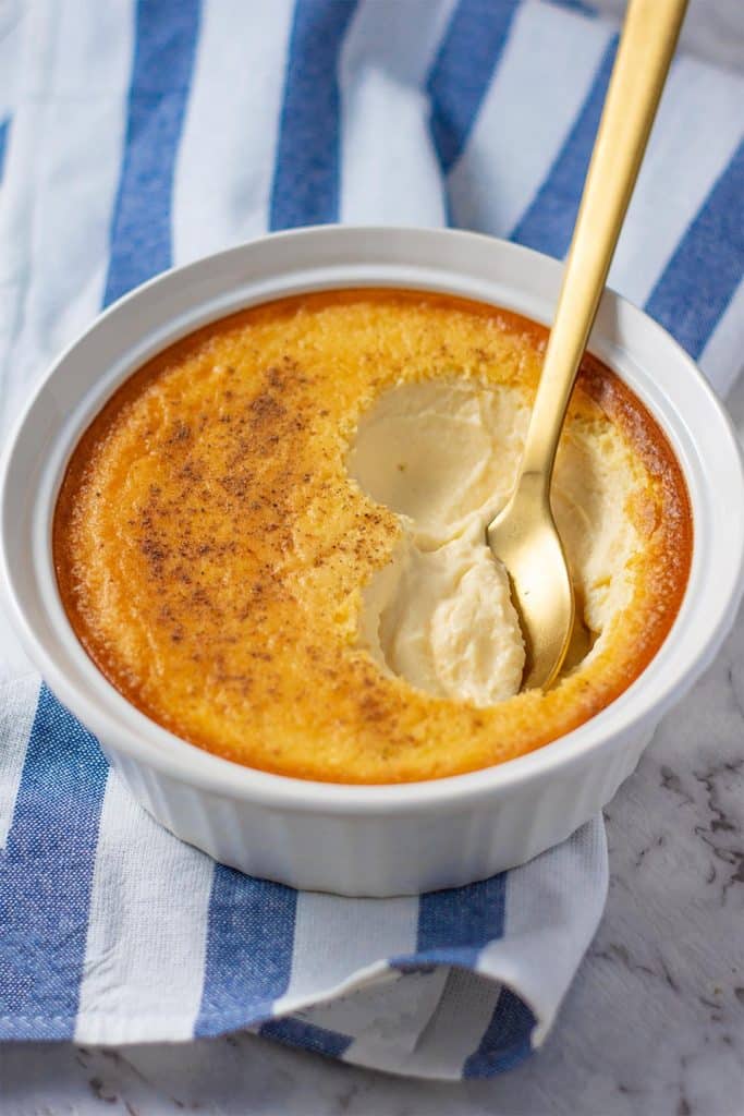 Keto custard in a bowl with a spoon a blue and white stripe tea towel.