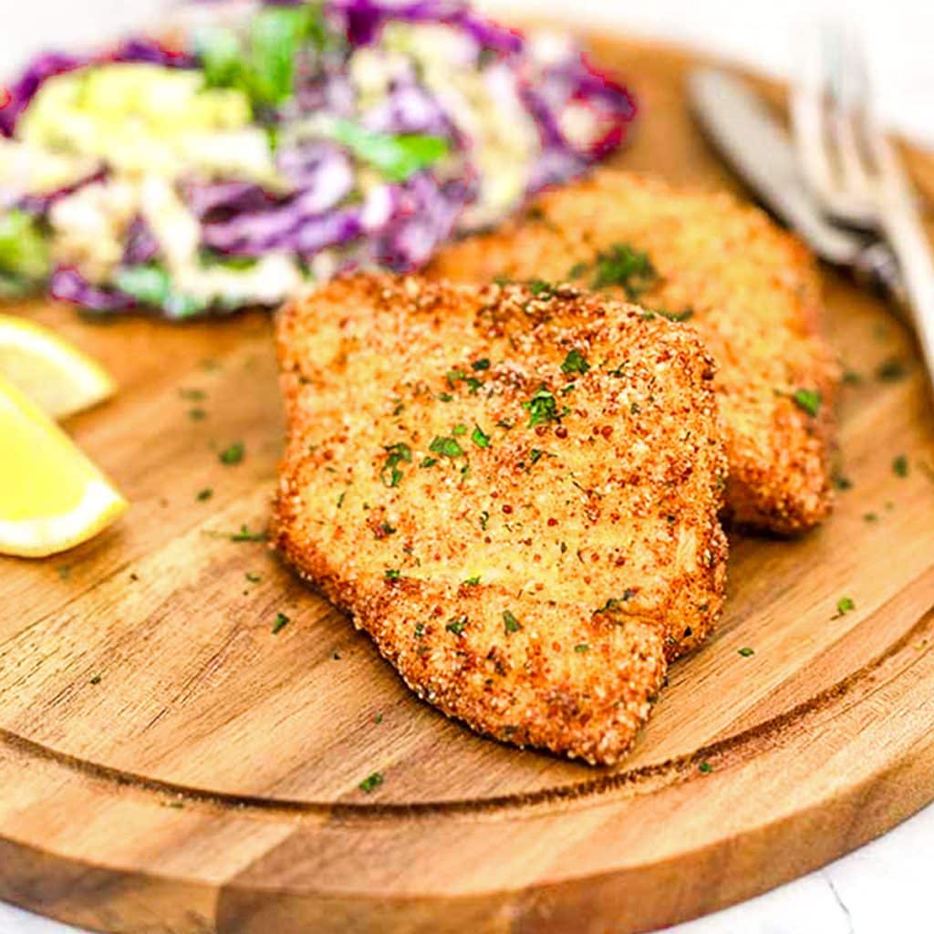 Keto breaded fish on a serving board with lemon wedges and coleslaw.