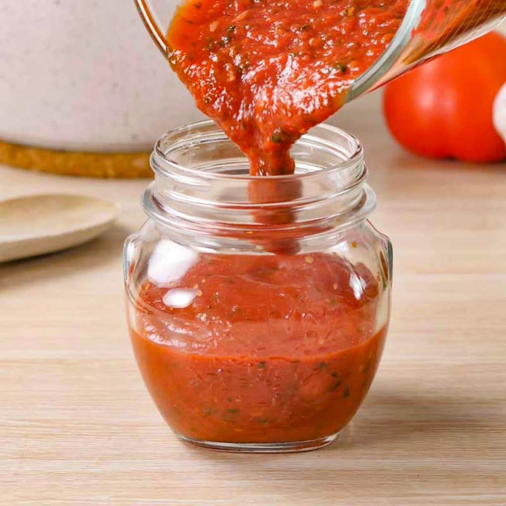Keto pizza sauce being poured into a jar.