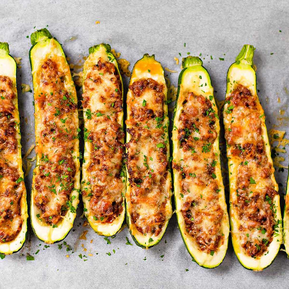 picture of 6 zucchini halves filled with ground beef on a grey background.