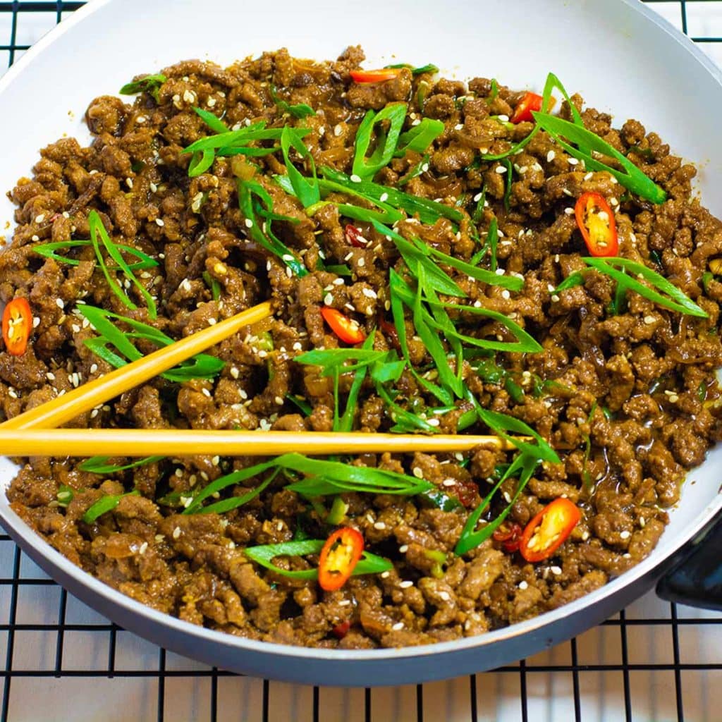 Sticky beef i a white bowl with chopsticks.