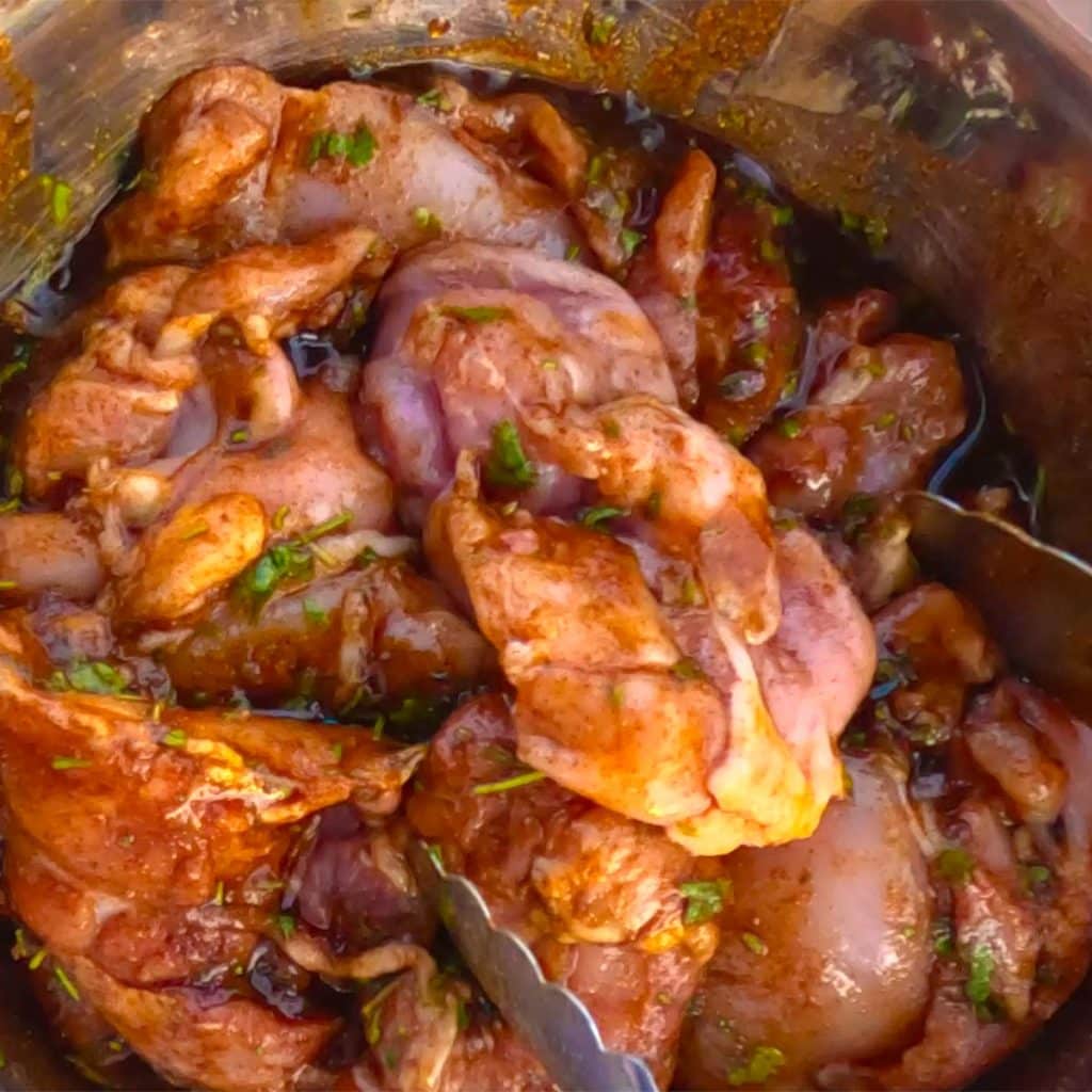 Boneless chicken thighs coated in marinade in a silver mixing bowl.